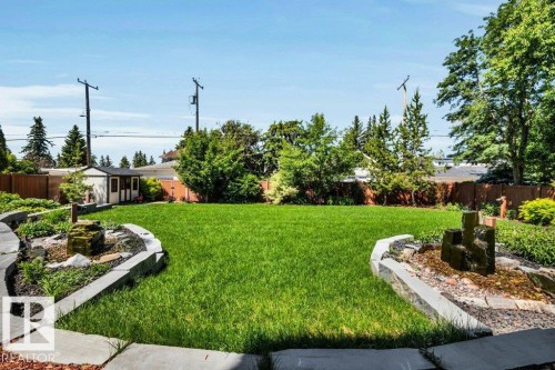 Expansive grassy yard featuring stone-bordered garden beds, a built-in water feature, and a storage shed - 8914 120 Street, Edmonton, AB 