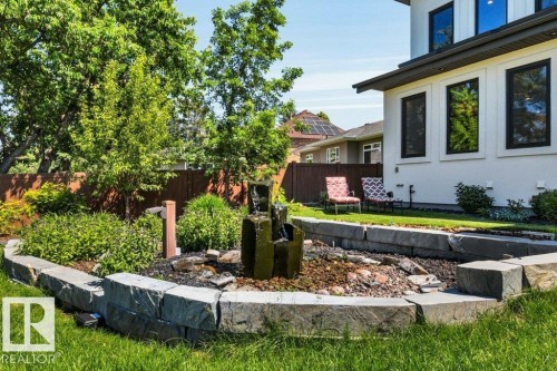 Landscaped garden bed featuring a tiered stone water feature, natural stone block retaining wall, and verdant plantings - 8914 120 Street, Edmonton, AB 