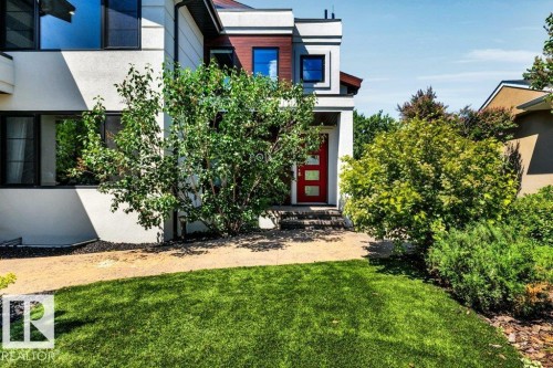 Modern architectural exterior featuring a prominent red entry door with frosted glass inserts, a flat roofline, and contrasting white stucco and wood-finish siding - 8914 120 Street, Edmonton, AB 
