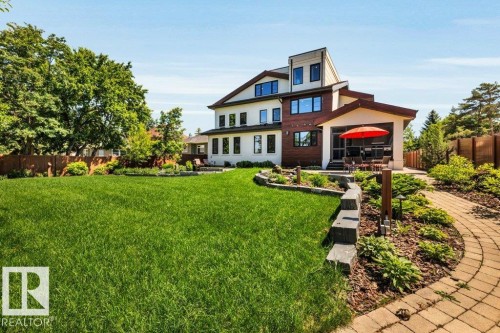 Expansive green lawn with a paver pathway leading to a multi-level home featuring white siding, wood panel accents, and a covered patio area - 8914 120 Street, Edmonton, AB 
