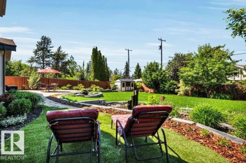 Expansive backyard featuring a stone patio, manicured lawn, tiered landscaping, wood fencing, and a storage shed - 8914 120 Street, Edmonton, AB 