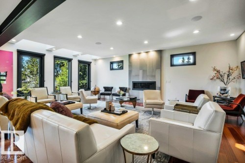 Spacious living area featuring rich wood-finish flooring, a contemporary fireplace with a stone-clad surround, multiple recessed lights, and large windows with black frames - 8914 120 Street, Edmonton, AB 