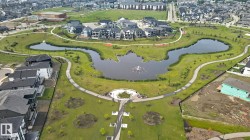 Expansive green space featuring a central pond with fountain, winding paved pathways, and surrounding residential structures - 