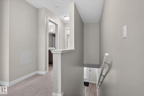 Neutral-toned walls complement the light carpeting in this upper-level hallway, featuring white trim and a white banister - #90 2560 Pegasus Bv Nw, Edmonton, AB - Indoor Photo Showing Other Room