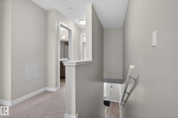 Neutral-toned walls complement the light carpeting in this upper-level hallway, featuring white trim and a white banister - 