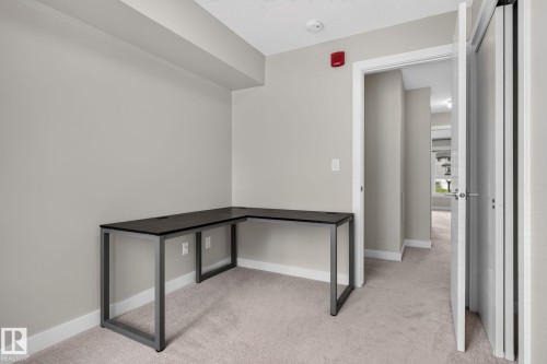 Flexible room featuring soft gray walls, neutral carpet, white trim, and a built-in L-shaped dark wood-finish desk with metal legs - #90 2560 Pegasus Bv Nw, Edmonton, AB - Indoor Photo Showing Other Room