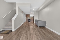 Open-concept living area featuring wood-finish flooring, a carpeted staircase with white railings, and light gray walls - 