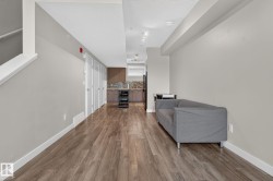 Open concept living area featuring wood-finish flooring, light gray walls, built-in shelving, and a kitchen with dark cabinetry and a tile backsplash - 