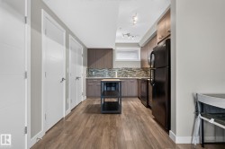 Modern kitchen featuring wood-finish flooring, two-tone cabinetry, a mosaic tile backsplash, black appliances, and a movable island with a wood countertop - 