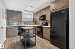Modern kitchen featuring wood-finish cabinetry, light-toned countertops, and a full suite of black appliances - 