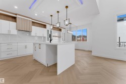 Open-concept kitchen featuring an island, white cabinetry with gold-toned hardware, chevron wood-finish flooring, and pendant lighting - 