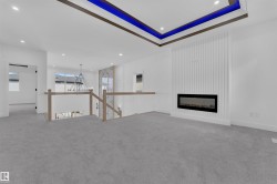 Spacious room featuring gray carpet, a contemporary electric fireplace with a vertically paneled surround, and a tray ceiling with integrated blue accent lighting - 