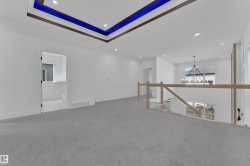 Open loft area featuring gray carpet flooring, a contemporary wood and glass railing, and a tray ceiling with recessed lighting and accent illumination - 
