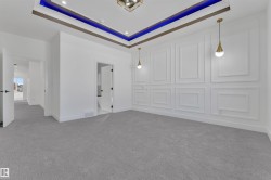 Recessed ceiling with blue accent lighting, a feature wall with decorative panel molding, and two pendant light fixtures - 