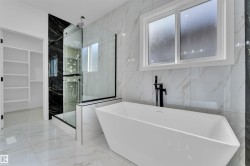 Freestanding soaking tub with a matte black floor-mounted faucet, complemented by a walk-in shower with a glass enclosure and black marble-look accent wall - 