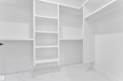Custom closet system with multiple shelving units and hanging rods, featuring white cabinetry and light-toned tile flooring - 
