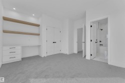 Spacious room featuring light gray carpeting, recessed lighting, and a built-in desk with white cabinetry, matte black hardware, and two wood-finish floating shelves - 