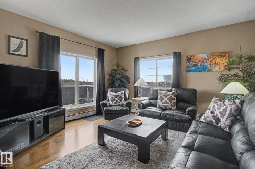 Spacious living area featuring wood-finish flooring, neutral wall tones, and multiple windows - 415 263 Macewan Road, Edmonton, AB 