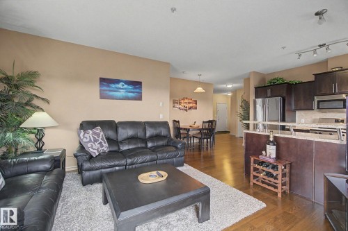 Open-concept living space featuring wood-finish flooring, a kitchen with dark wood cabinetry, stainless steel appliances, a breakfast bar, and a dining area - 415 263 Macewan Road, Edmonton, AB 