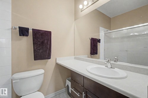 Bathroom featuring a dark wood-finish vanity with a light-toned countertop, an integrated sink with a chrome faucet, and a large mirror - 415 263 Macewan Road, Edmonton, AB 