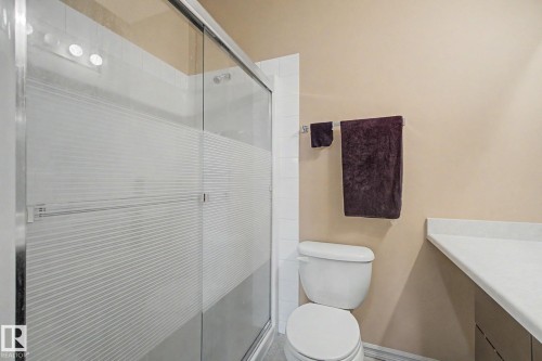 Bathroom featuring a sliding glass shower enclosure with frosted privacy bands, white subway tile shower surround, a white toilet, and a light-colored countertop - 415 263 Macewan Road, Edmonton, AB 