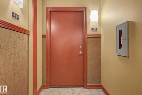 Entryway featuring a solid panel door, wainscoting with a patterned finish, wall-mounted sconces, and neutral wall paint - 415 263 Macewan Road, Edmonton, AB 