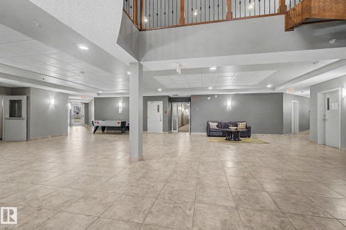 Spacious common area featuring large format tile flooring, recessed lighting, wall sconces, and a multi-level design with a visible upper floor railing - 415 263 Macewan Road, Edmonton, AB 