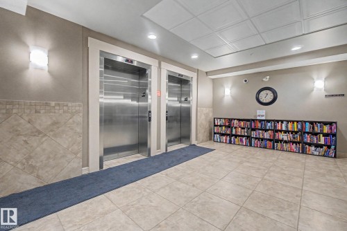 Dual stainless steel elevators set within a tiled lobby space featuring recessed lighting, wall sconces, and a textured ceiling - 415 263 Macewan Road, Edmonton, AB 
