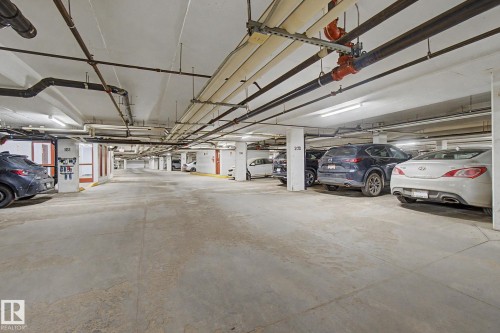 Underground parking facility with concrete flooring, exposed overhead piping, and fluorescent lighting - 415 263 Macewan Road, Edmonton, AB 
