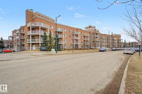 Multi-story brick building featuring multiple private balconies, architectural cornices, and landscaped grounds with mature evergreen trees - 415 263 Macewan Road, Edmonton, AB 