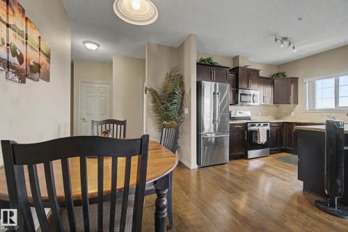 Open-concept kitchen featuring dark wood cabinetry, stainless steel appliances, granite countertops, and wood-finish flooring - 415 263 Macewan Road, Edmonton, AB 