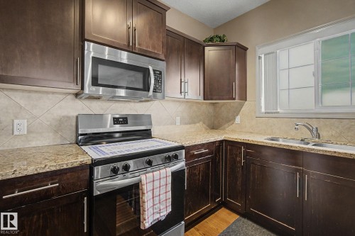 Kitchen featuring dark wood-finish cabinetry, light-toned countertops, and stainless steel appliances including a range and microwave - 415 263 Macewan Road, Edmonton, AB 