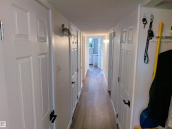 Hallway featuring wood-finish flooring, white paneled doors, and contemporary wall sconce lighting - 
