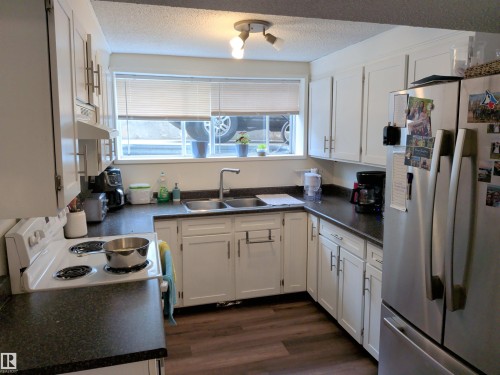 Kitchen featuring white cabinetry, dark countertops, wood-finish flooring, a double basin sink, and a stainless steel refrigerator - 31 Brown Street, Stony Plain, AB 