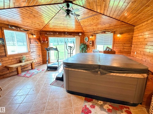 Spacious room featuring a large, covered hot tub, tongue-and-groove wood paneling on walls and ceiling, a ceiling fan with integrated lighting, multiple windows providing natural light, and tile flooring - 26418 Twp Rd 633, Rural Westlock County, AB 