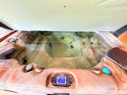Outdoor spa featuring a textured wood-finish exterior, integrated control panel, multiple jets, and an open cover - 