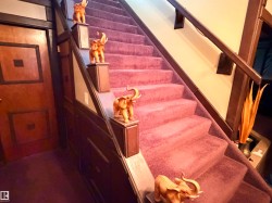 Staircase featuring plush carpet, wood-paneled walls, a solid wood entry door, and a dark wood handrail - 