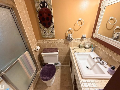 Bathroom featuring a tiled shower enclosure, a white vanity with an integrated sink, a chrome faucet, a wall-mounted mirror, and tile flooring - 26418 Twp Rd 633, Rural Westlock County, AB 