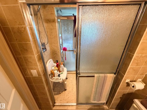 Shower enclosure featuring textured glass sliding doors, chrome hardware, and full-height neutral-toned tile surround - 26418 Twp Rd 633, Rural Westlock County, AB 