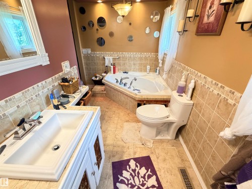 Bathroom featuring a corner jetted tub, wall-mounted light fixture, tile flooring, tile wainscoting, and a single vanity with a white basin - 26418 Twp Rd 633, Rural Westlock County, AB 