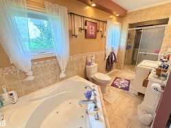 Tiled bathroom with a built-in jetted tub, separate shower enclosure with sliding glass doors, double vanity, and window - 