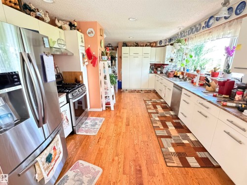 Kitchen featuring wood-finish flooring, white cabinetry, and stainless steel appliances - 26418 Twp Rd 633, Rural Westlock County, AB 