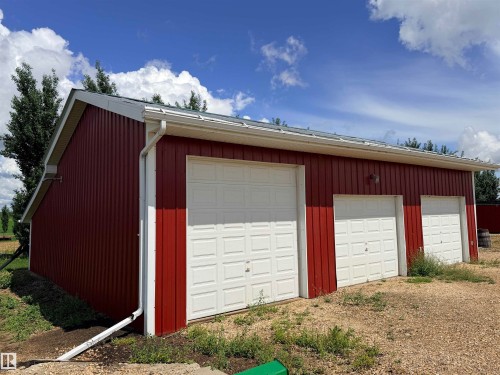 Red corrugated siding building featuring three white paneled garage doors - 26418 Twp Rd 633, Rural Westlock County, AB 