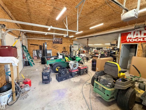 Spacious utility garage featuring an overhead door, exposed wood-finish paneling on walls and ceiling, concrete flooring, and fluorescent strip lighting - 26418 Twp Rd 633, Rural Westlock County, AB 