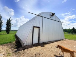 Corrugated metal quonset hut with a white entrance door, a gravel approach, and exterior lighting - 