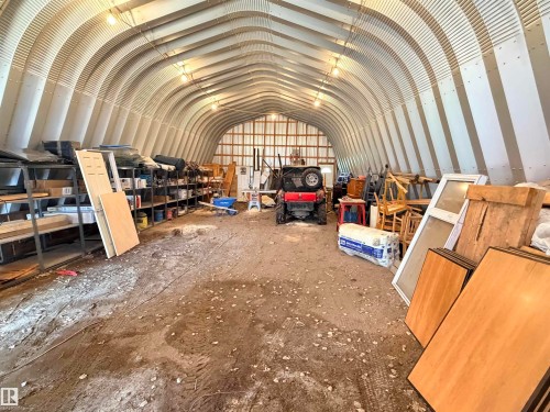 Quonset hut structure featuring an arched metal roof, exposed interior framing, dirt flooring, and overhead lighting - 26418 Twp Rd 633, Rural Westlock County, AB 