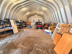 Quonset hut structure featuring an arched metal roof, exposed interior framing, dirt flooring, and overhead lighting - 