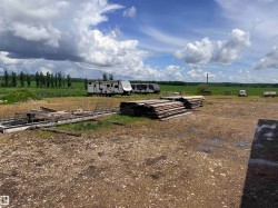 Expansive open lot with a gravel and dirt surface, featuring stacked timber and concrete forms - 