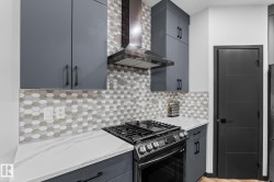 Modern kitchen featuring dark gray cabinetry with matte black hardware, white veined countertops, and a full-height geometric tile backsplash - 