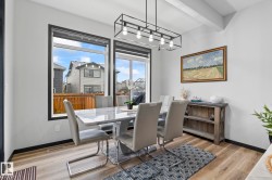 Dining area featuring large windows with dark trim, wood-finish flooring, and a contemporary linear chandelier with exposed bulbs - 